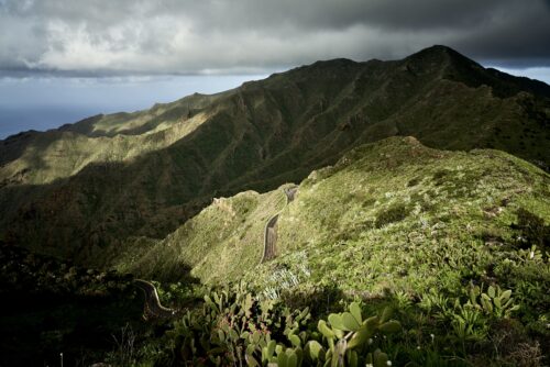 Color photography showing bird view on green hills and mountains with a small road beneath